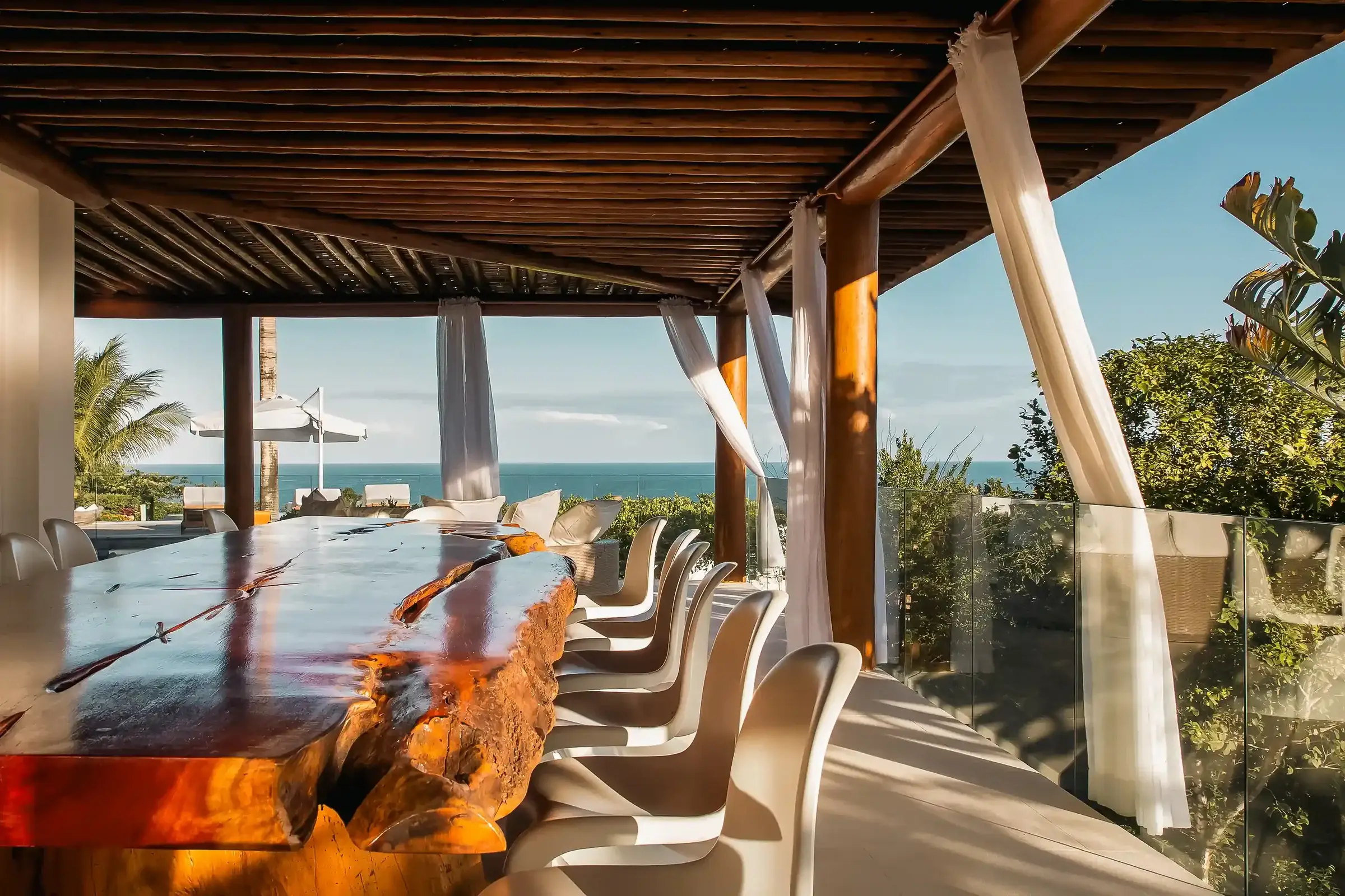 Wooden dining table under the pergola, pool and sea behind at Villa Greda