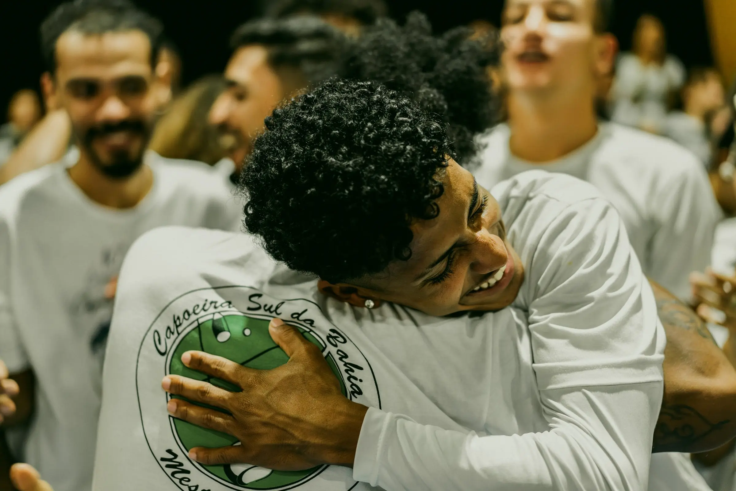Capoeiristas de branco se abraçando e sorrindo após a roda