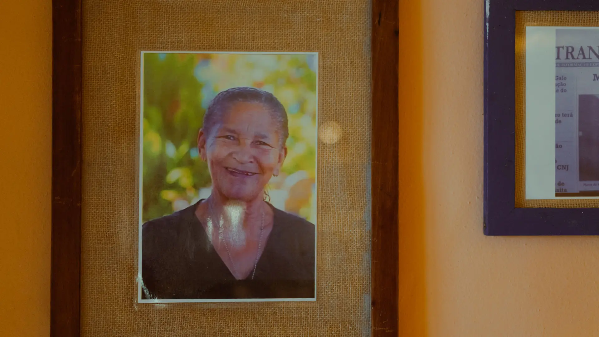 Retrato emoldurado de uma mulher idosa sorrindo, pendurado numa parede de estuque