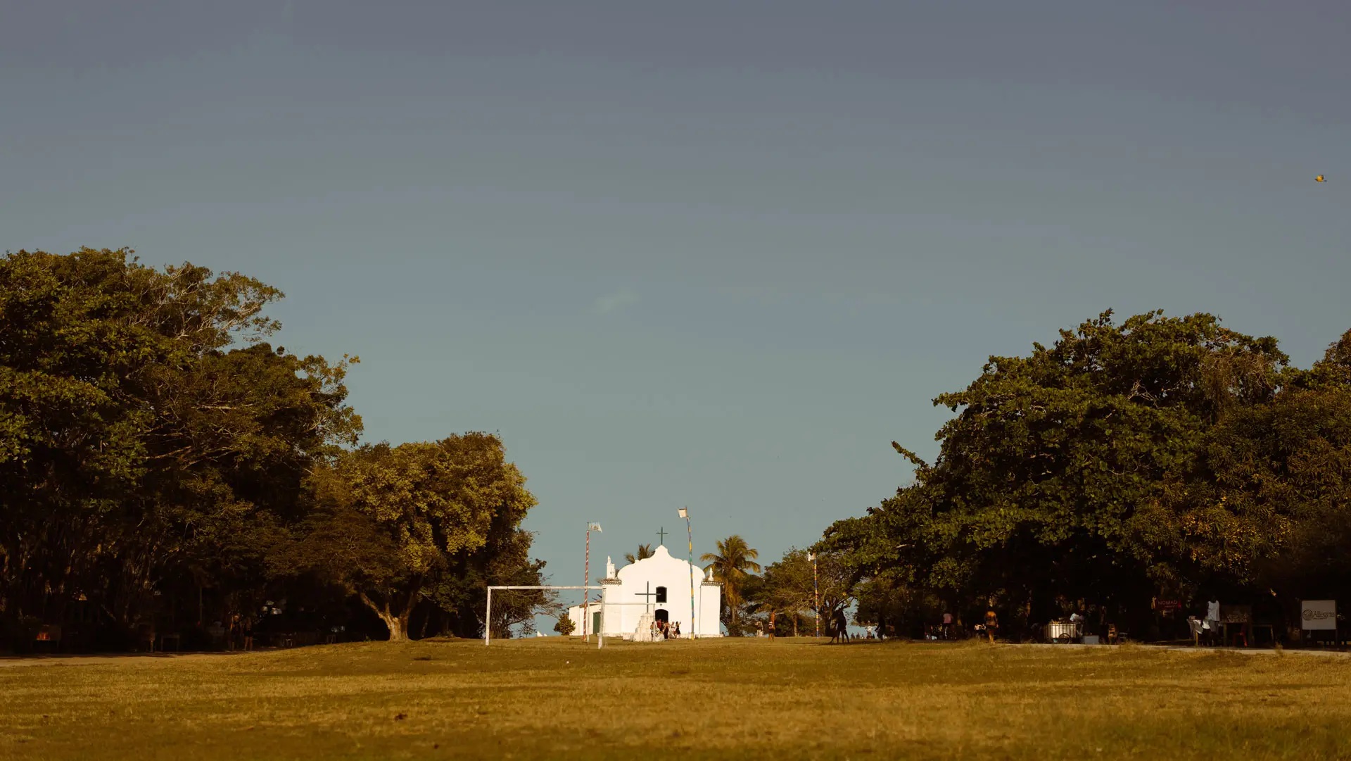Gramado do Quadrado de Trancoso com a igreja branca ao fundo entre árvores
