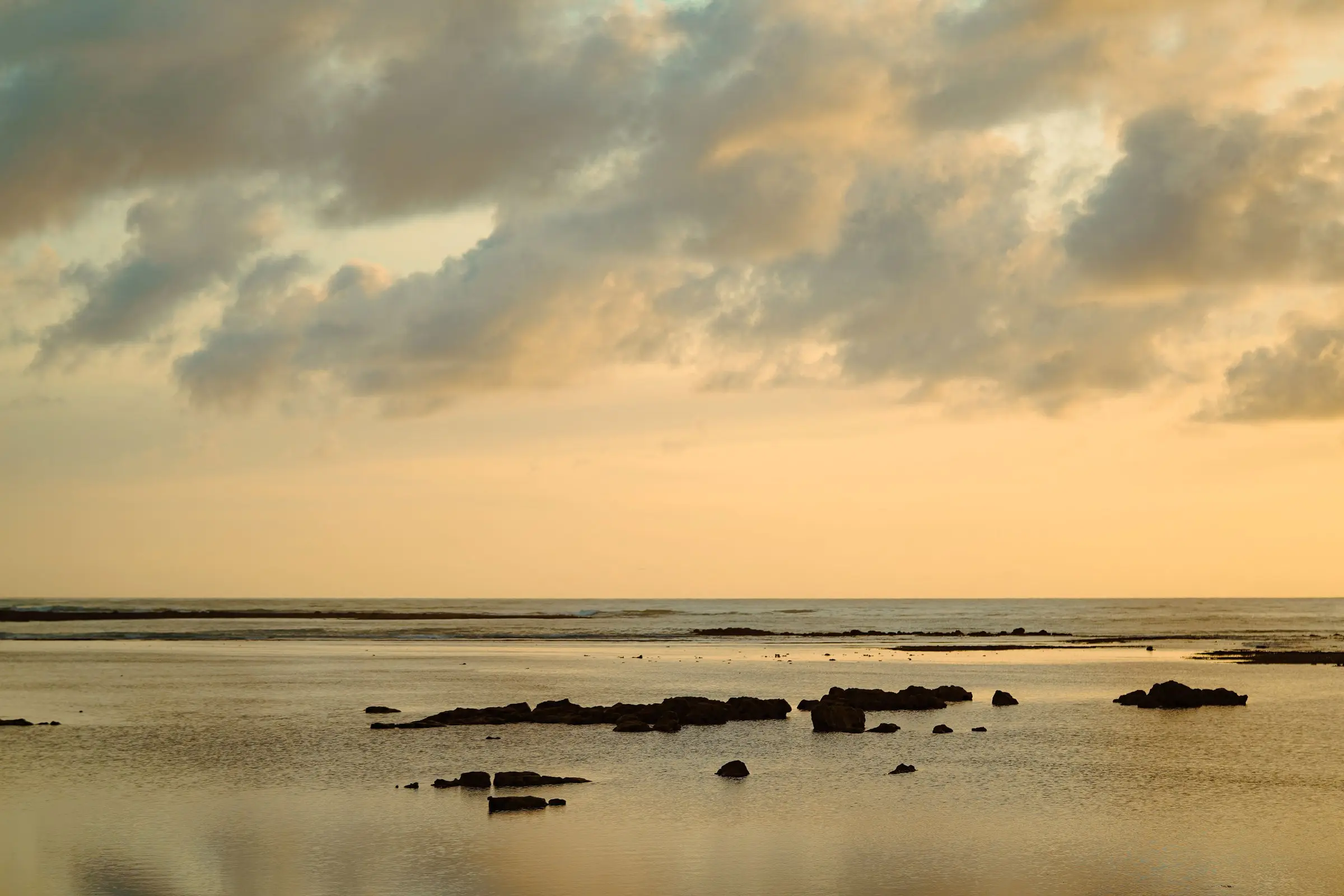 Piscinas naturais em rochas ao pôr do sol, mar calmo e céu nublado