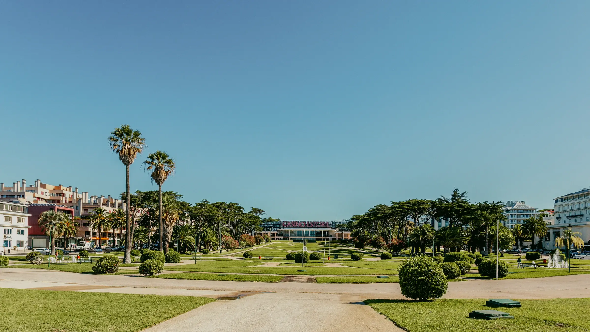 Jardins do Casino Estoril, com palmeiras e canteiros, vistos da Praia do Tamariz