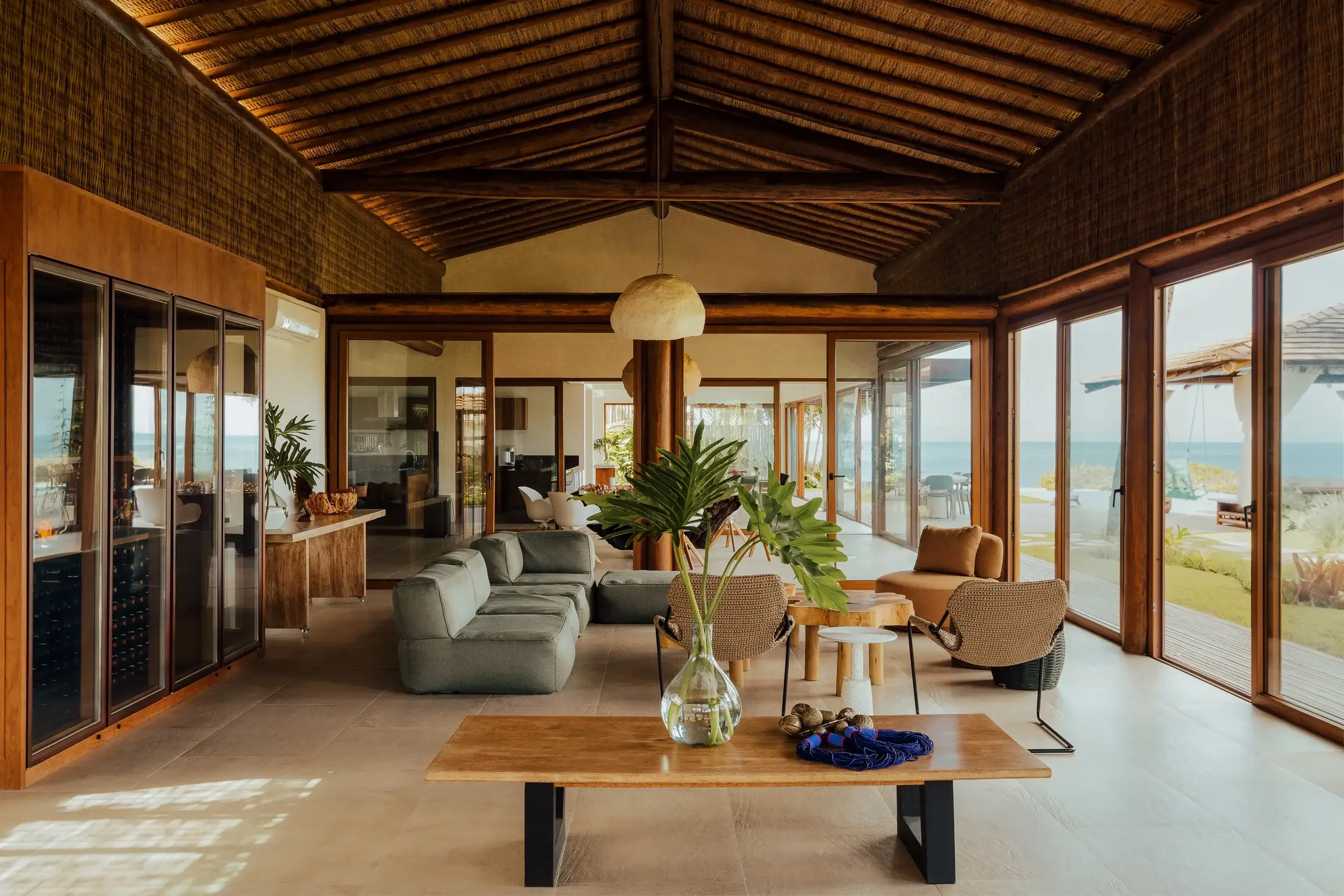 Living room with a thatched ceiling, sofas and a wooden table, open to the sea