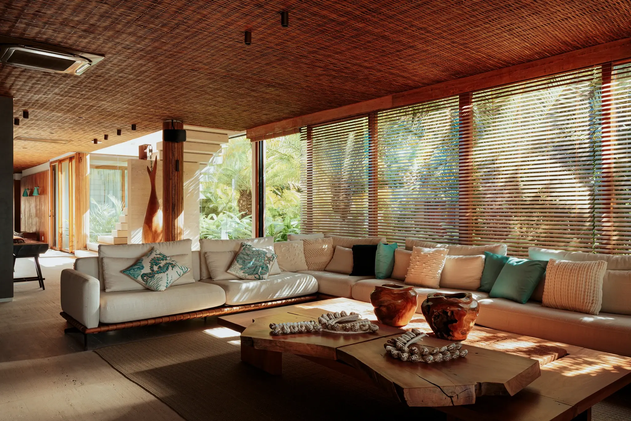 Open living room at Falésia, with an L-shaped sofa, a log table and a straw ceiling