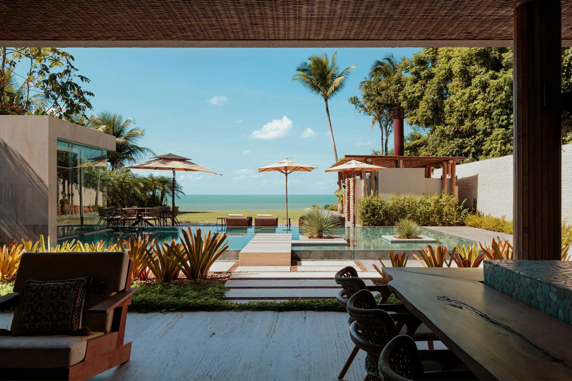 View from the straw-covered veranda towards the pool, the parasols and the sea, at Falésia