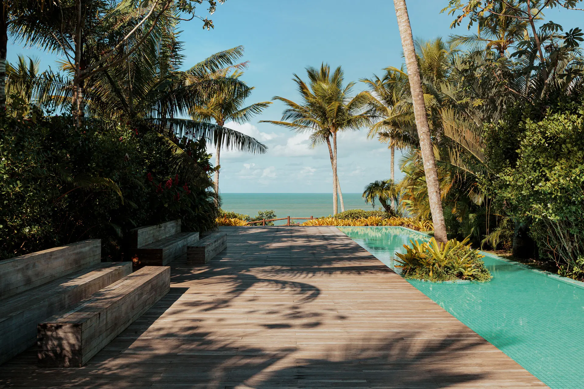 Long pool beside the wooden deck, with the beach and palm trees behind