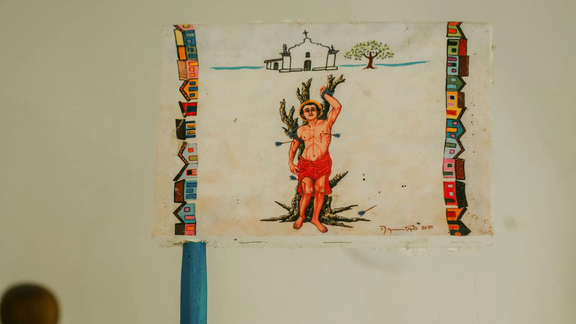 Bandeira pintada por Damião com a figura de um santo, pendurada na parede do ateliê