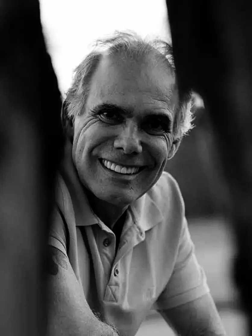 Luiz Carlos Orsini, landscape designer, smiling among tree trunks, in black and white
