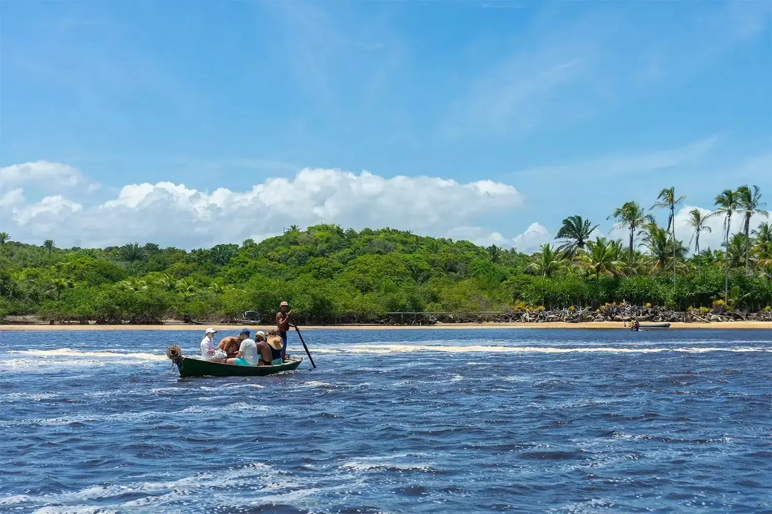 Canoe with passengers crossing the Caraíva river, village and palms on the far bank