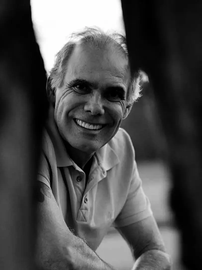 Luiz Carlos Orsini, Brisa's landscape designer, leaning on a trunk, in black and white