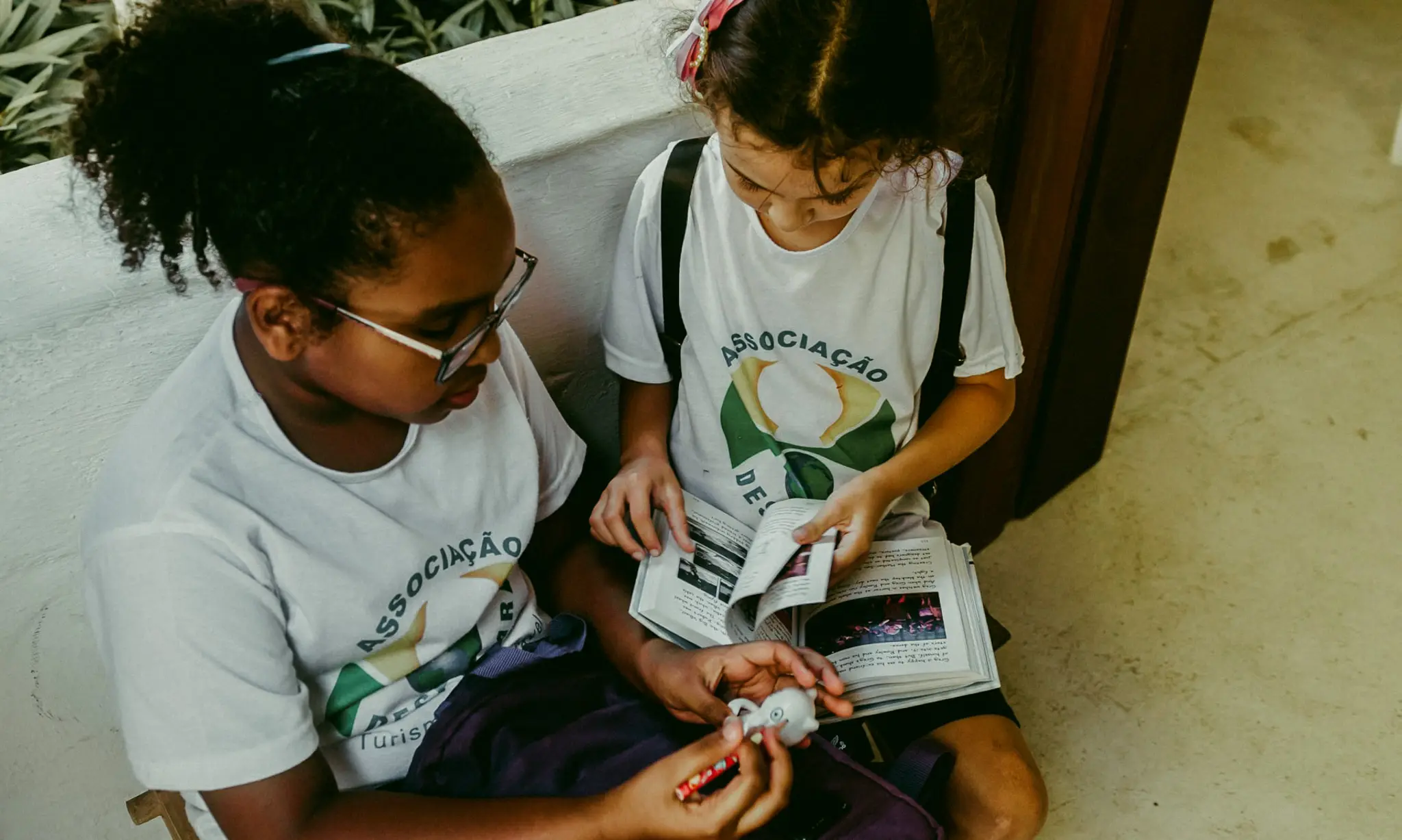 Duas crianças lendo juntas sentadas no chão, com camisetas da Associação Despertar