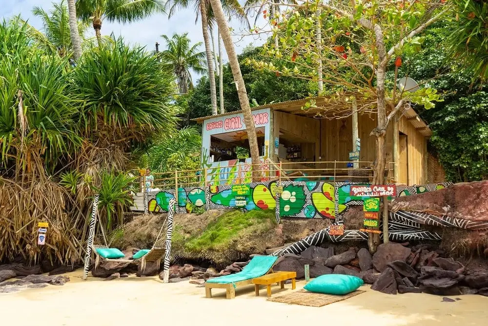 Beach hut with colourful graffiti and loungers under palm trees