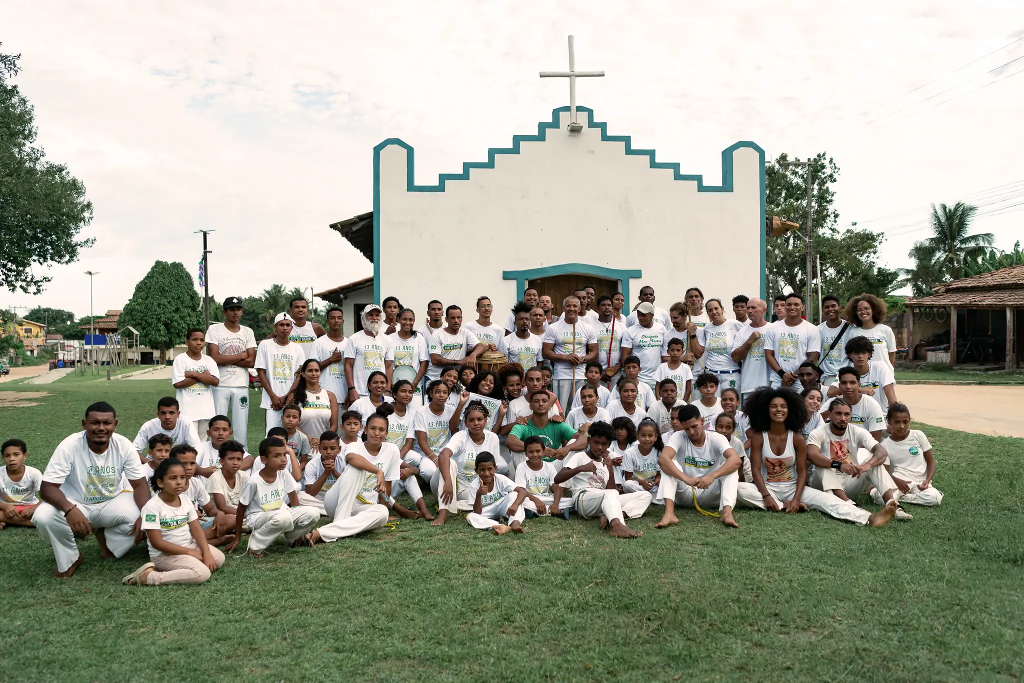 Grupo de capoeira reunido, de branco, diante da igreja de Trancoso