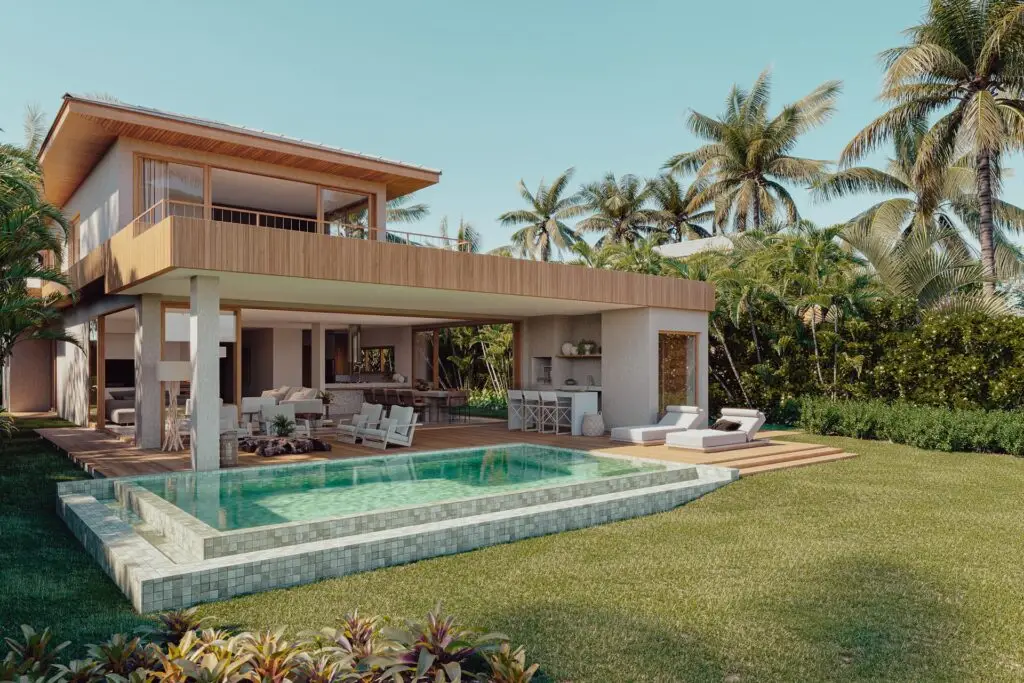 Uma casa de praia de alto padrão contemporânea em Trancoso possui um terraço aberto adornado com móveis de exterior e uma área para refeições. De frente para ela está uma piscina elegante emoldurada por um gramado verde vibrante, palmeiras ondulantes e uma variedade de flora tropical. O céu azul brilhante indica um dia ensolarado, ideal para se deliciar neste luxuoso retiro próximo a Arraial d'Ajuda.