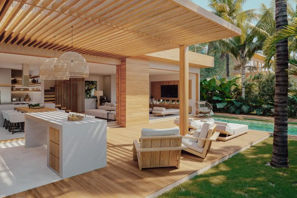 Uma casa de praia de alto padrão com pergolado de madeira, área de estar aconchegante com cadeiras e sofás macios, elegante bancada em ilha branca, detalhes em madeira clara e piscina cercada por vegetação exuberante e palmeiras altas - ideal para quem busca casas de praia de alto padrão em Trancoso ou Arraial d'Ajuda Nampur.