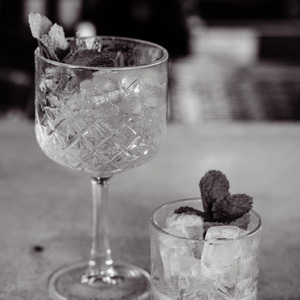 Elegantes copos de cristal com gelo e hortelã em uma mesa, cenário preto e branco, estilo casas de praia de alto padrão em Trancoso ou Arraial d'Ajuda.