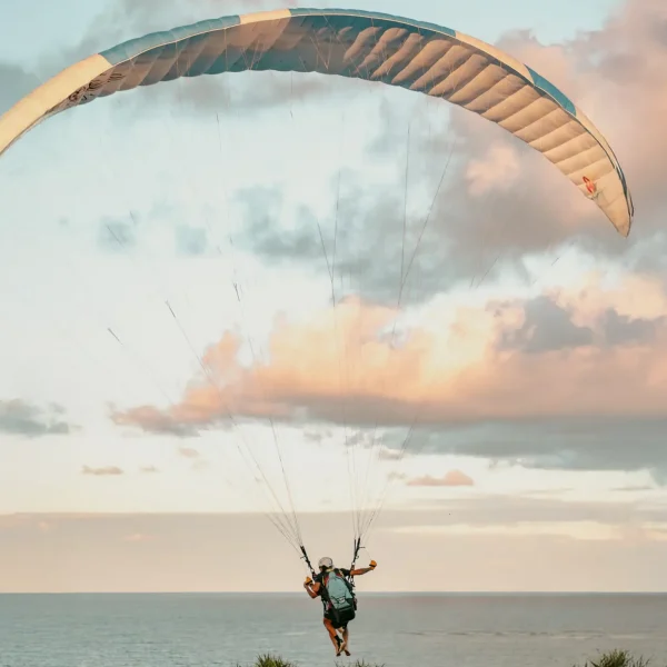 Paraglider soars above grassy terrain near casas de praia de alto padrão in Trancoso and Arraial d'Ajuda at sunset, pastel sky above.