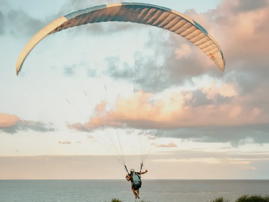 Paraglider soars above grassy terrain near casas de praia de alto padrão in Trancoso and Arraial d'Ajuda at sunset, pastel sky above.